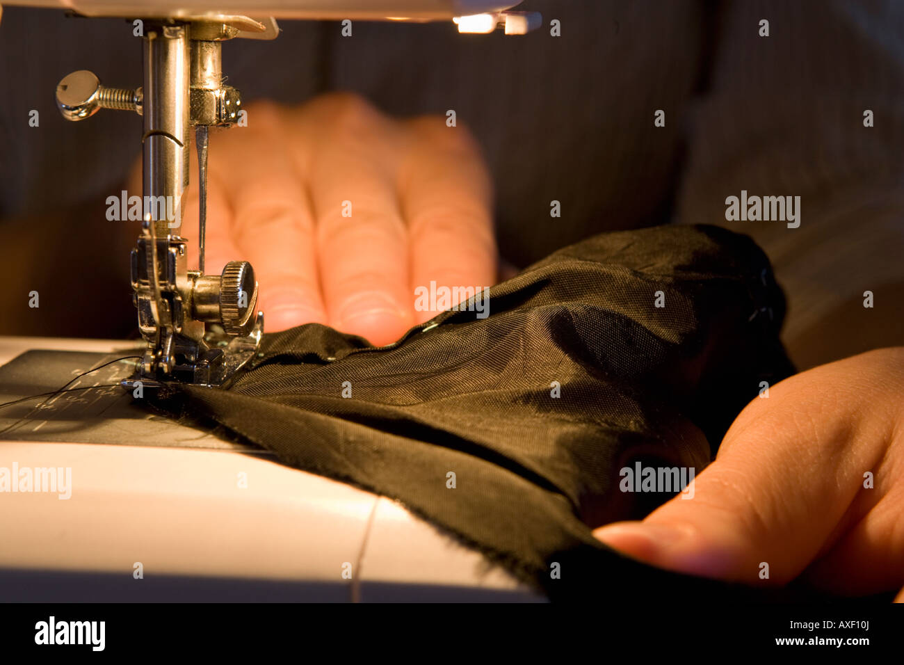 Close up of a woman using a sewing machine to stitch black fabric. With sharp focus on the needle and fabric. Stock Photo