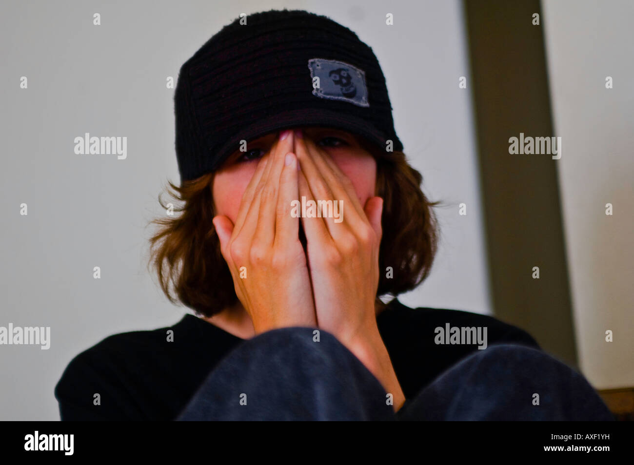 Young teenage boy with long hair and black cap hiding his face behind his  hands Stock Photo - Alamy