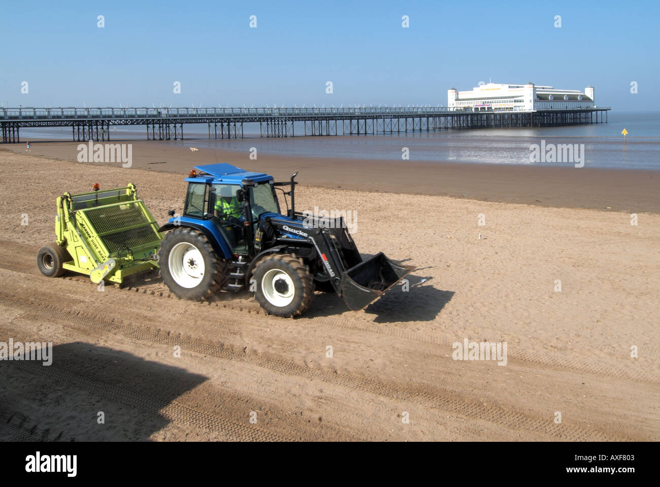 Weston Super Mare beach early morning tractor pulling litter collecting machine across sand before visitors arrive pier beyond Stock Photo