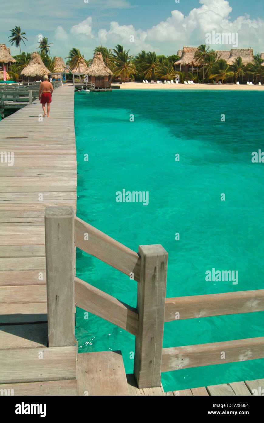 A long wooden pier juts into the Caribbean Sea from a tropical beach with thatched huts Stock Photo
