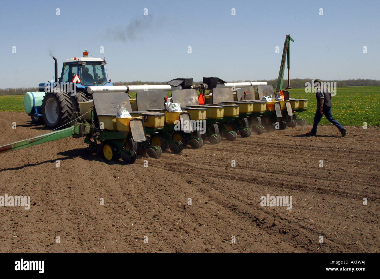 A farm worker walks being a tractor and planter ensuring the seed bins are working correctly and seeds are being planted. Stock Photo