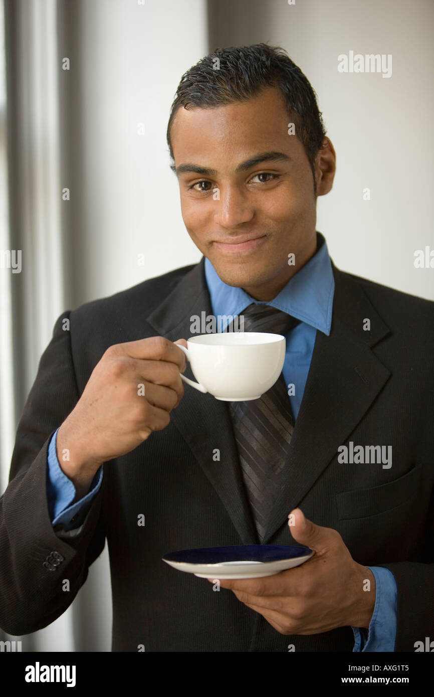 Smiling young business man drinking tea holding a cup and saucer and