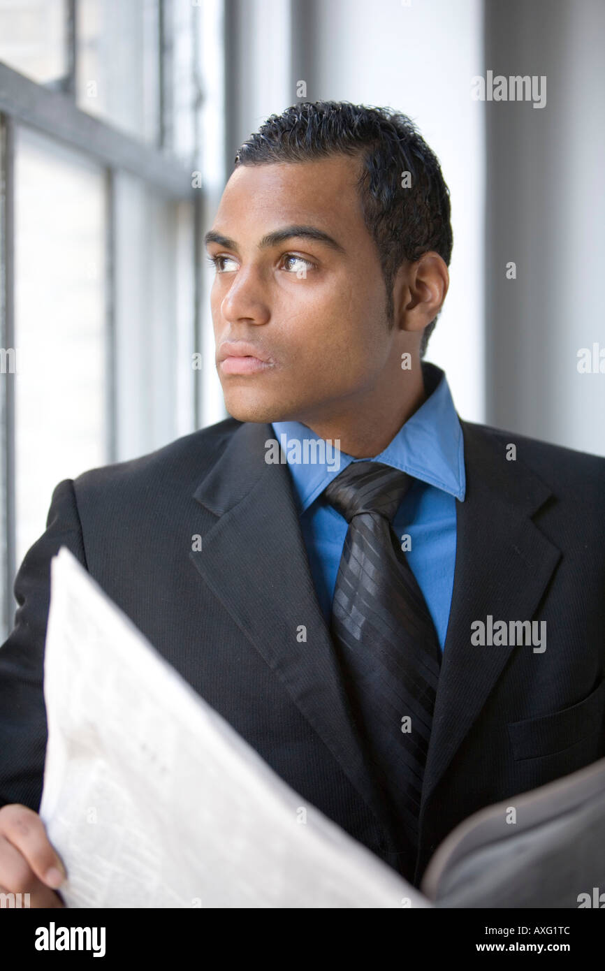 A young business man reading a newspaper by a window wearing a suit and time Stock Photo