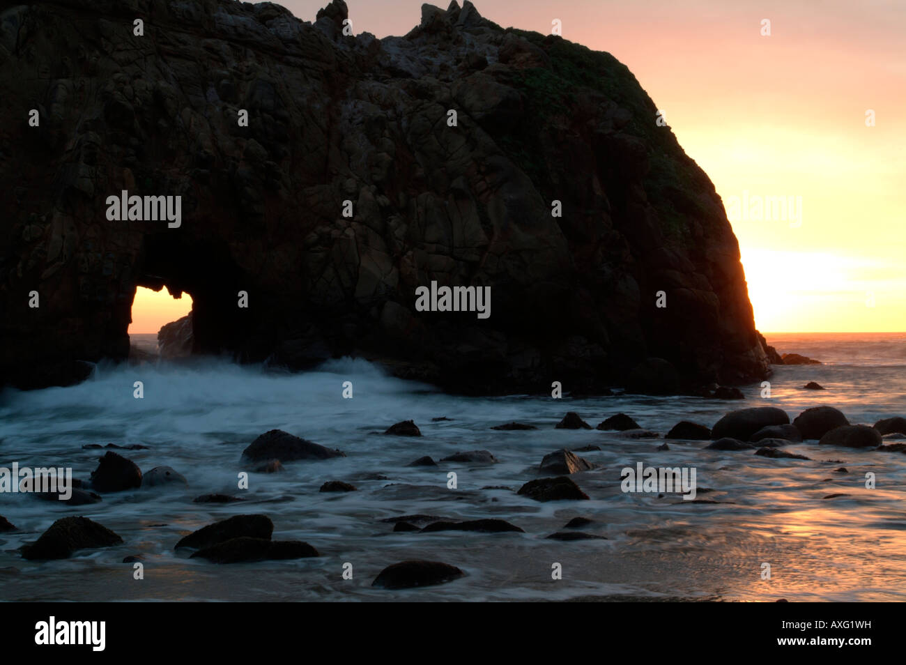 waves crashing through a sea arch at sunset on Pfeiffer beach along the ...
