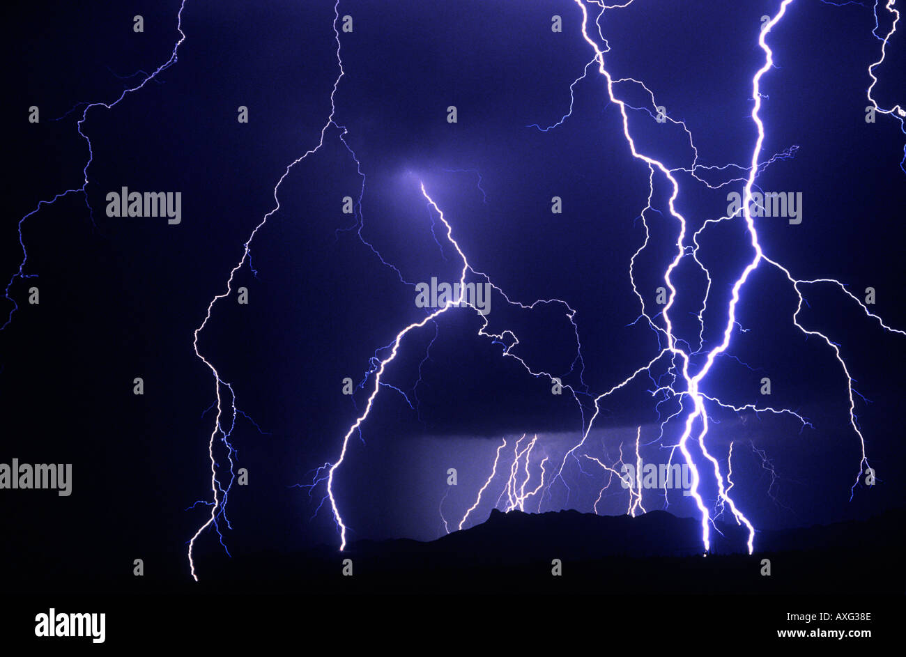 Multiple lightning bolts layer the sky at night over a desert mountain range. Stock Photo