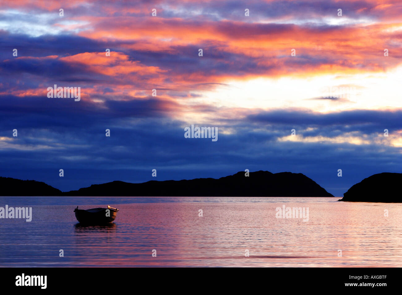 Sunset offshore Sheildaig on the west coast of Scotland with a single rowing boat moored in calm multi coloured water and skies Stock Photo