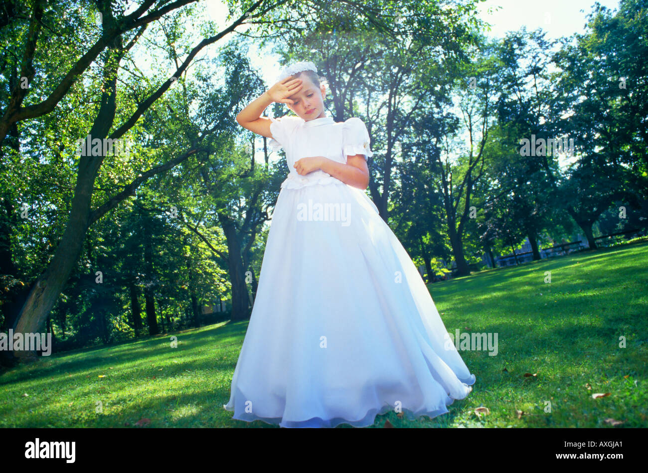 A little girl in a white dress and a wreath on her head standing in a ...