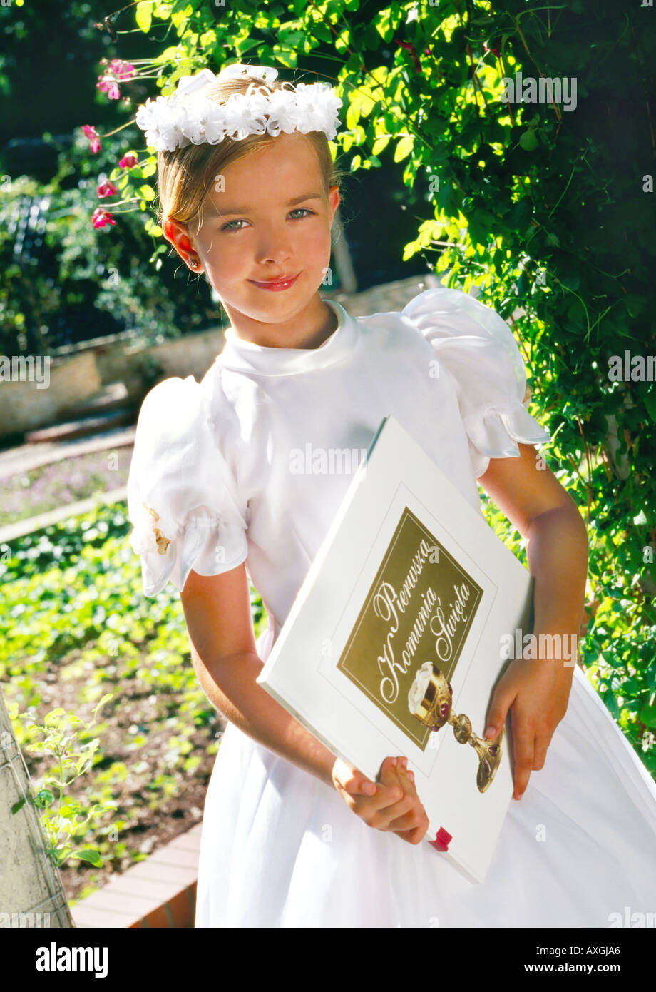 A little girl in a white dress and a wreath on her head standing in a ...