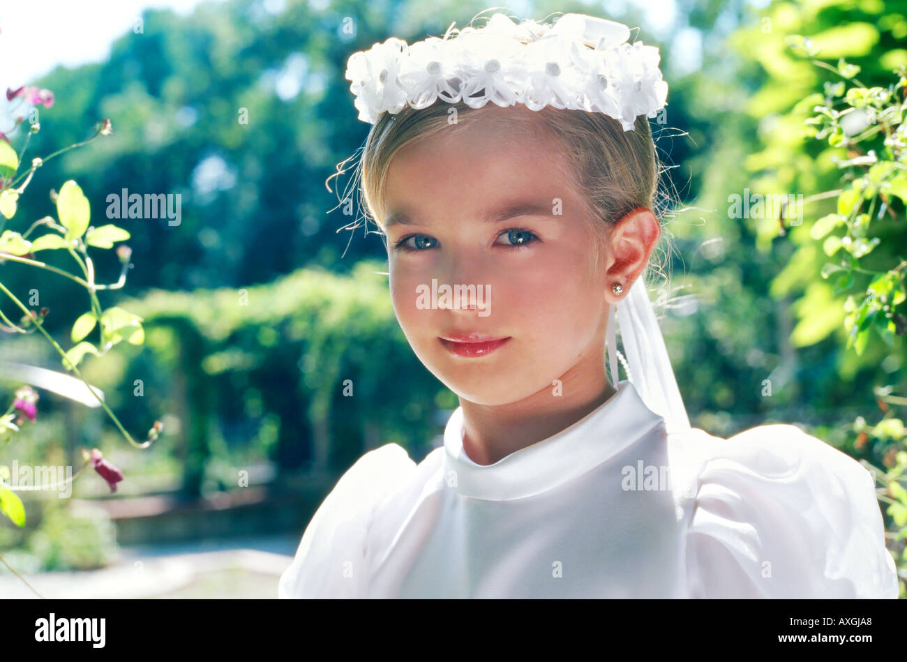 A little girl in a white dress and a wreath on her head standing in a ...