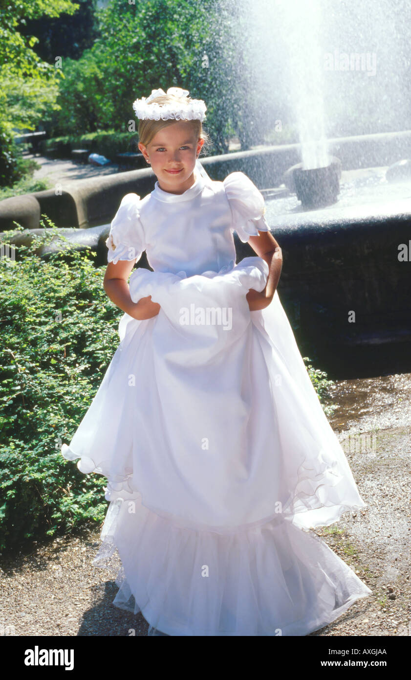 A little girl in a white dress and a wreath on her head standing in a ...