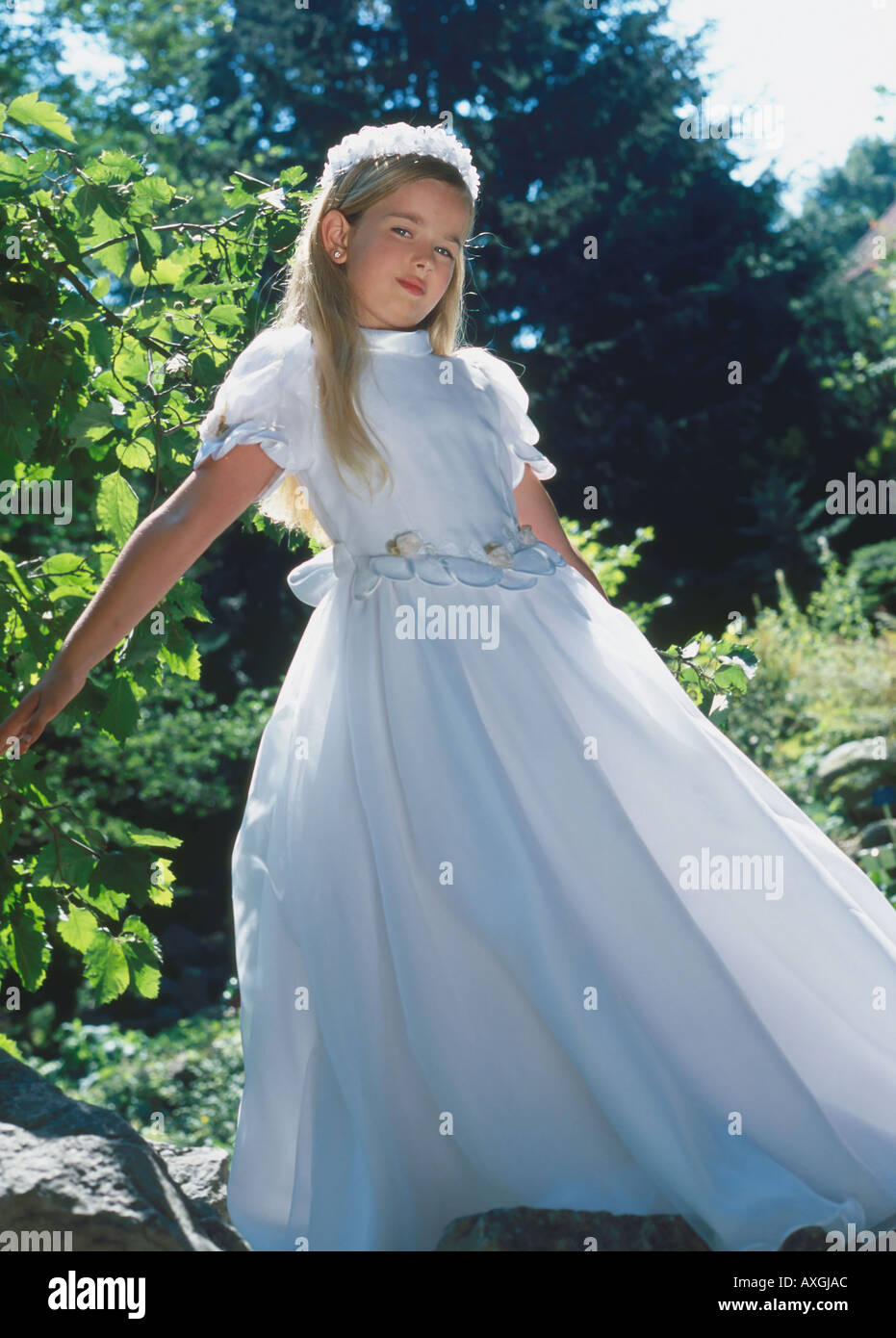 A little girl in a white dress and a wreath on her head standing in a ...