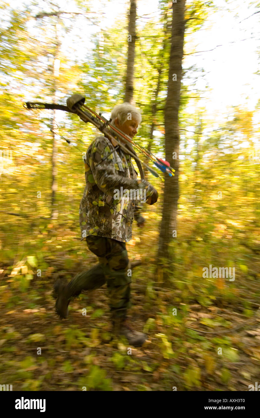 A WOMAN BOW HUNTER HUNTING WHITE TAIL DEER WALKS THROUGH THE WOODS WITH