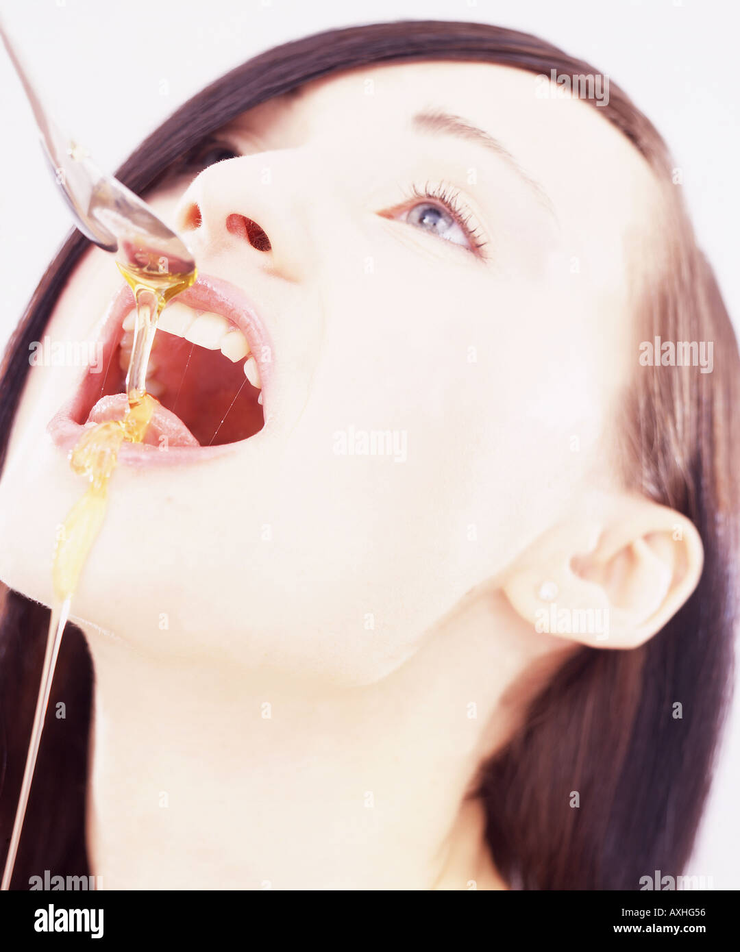 Portrait of a young woman eating honey which is dripping from a spoon. Stock Photo