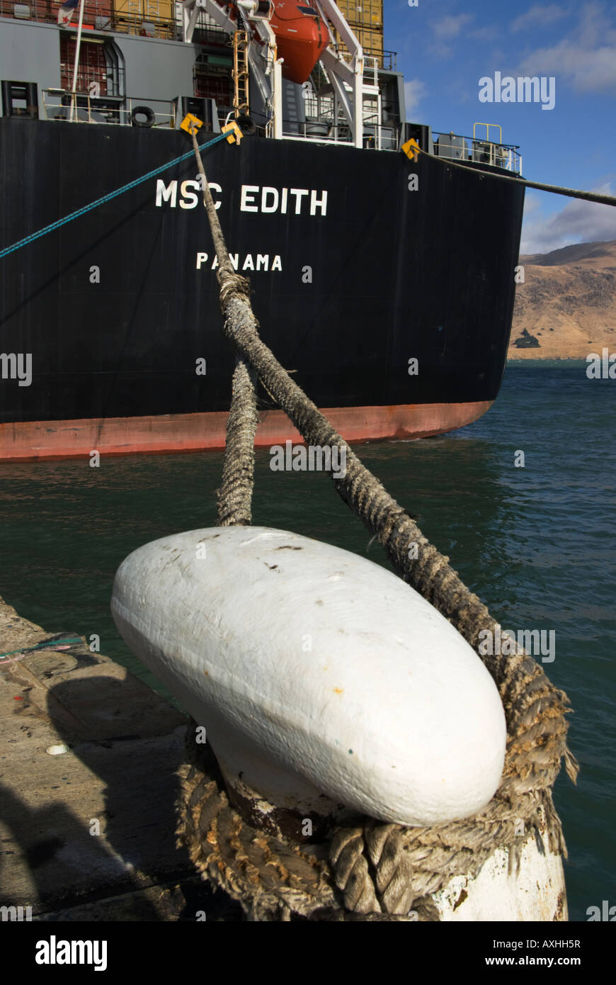 A mooring ropes securing the stern of a container ship to a shore bollard. Stock Photo