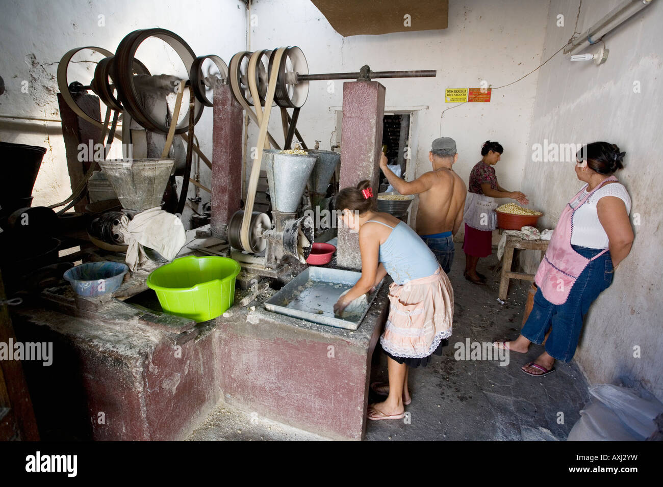 Women grinding grain into flour at a community molina aka mill in Suchitoto El Salvador while mechanic tends belts and pulleys Stock Photo