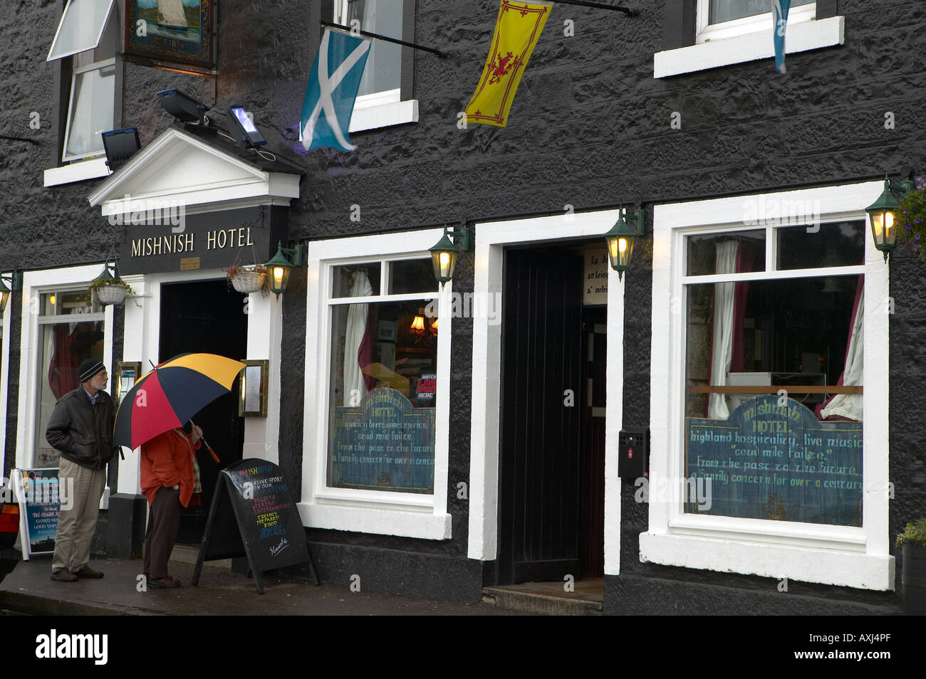 Tourists looking in on Mishnish pub and hotel on seafront, Tobermory, Isle of Mull, west coast of Scotland, United Kingdom Stock Photo