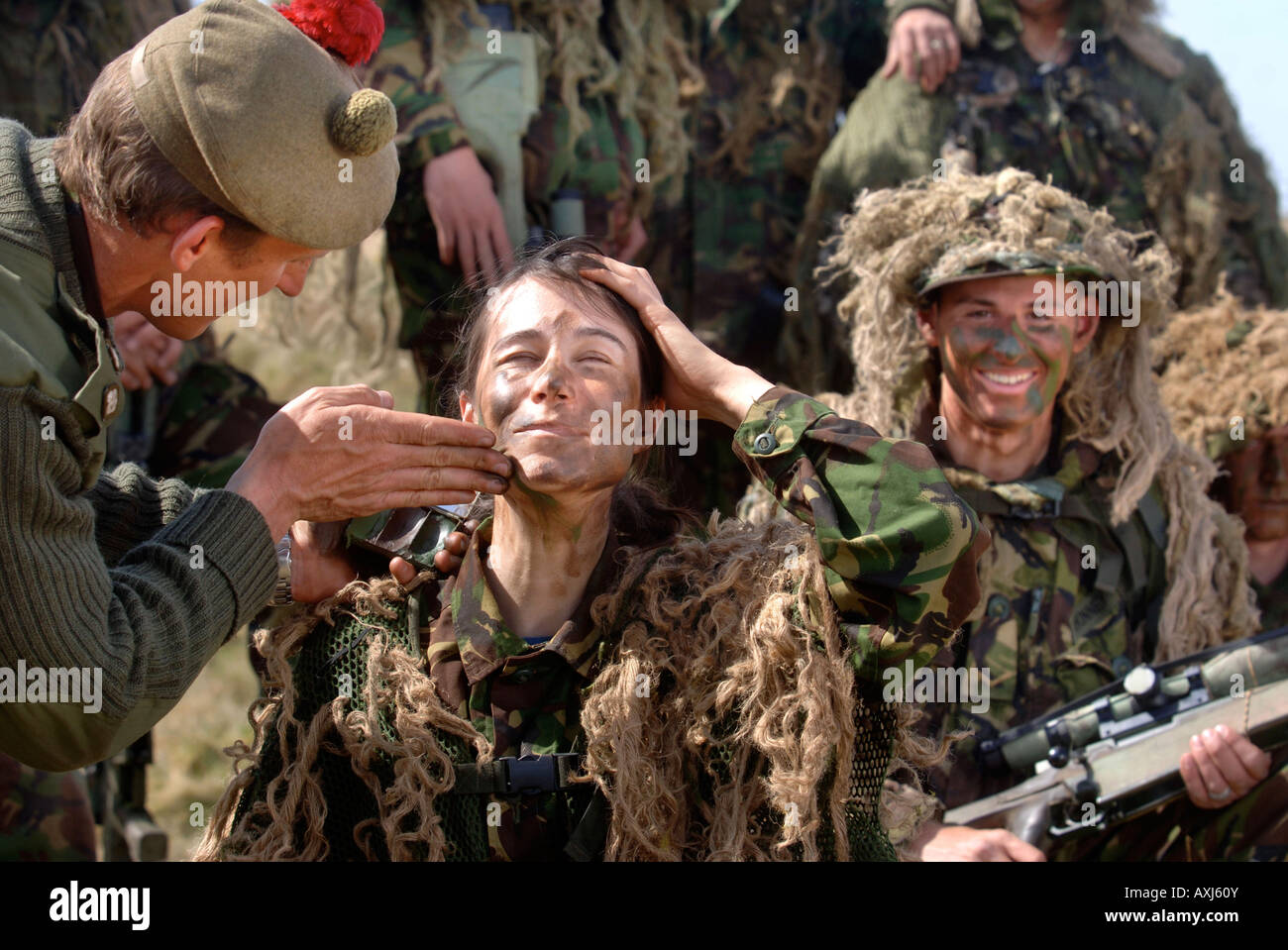 A BRITISH ARMY FEMALE RECRUIT HAS HELP SMEARING HER FACE WITH CAMOUFLAGE CREAM DURING A SNIPER TRAINING COURSE IN BRECON WALES Stock Photo
