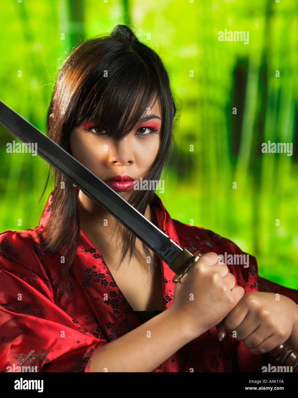 Asian tough fighting warrior girl holding sword diagonally with hair in eyes wearing red green background Stock Photo