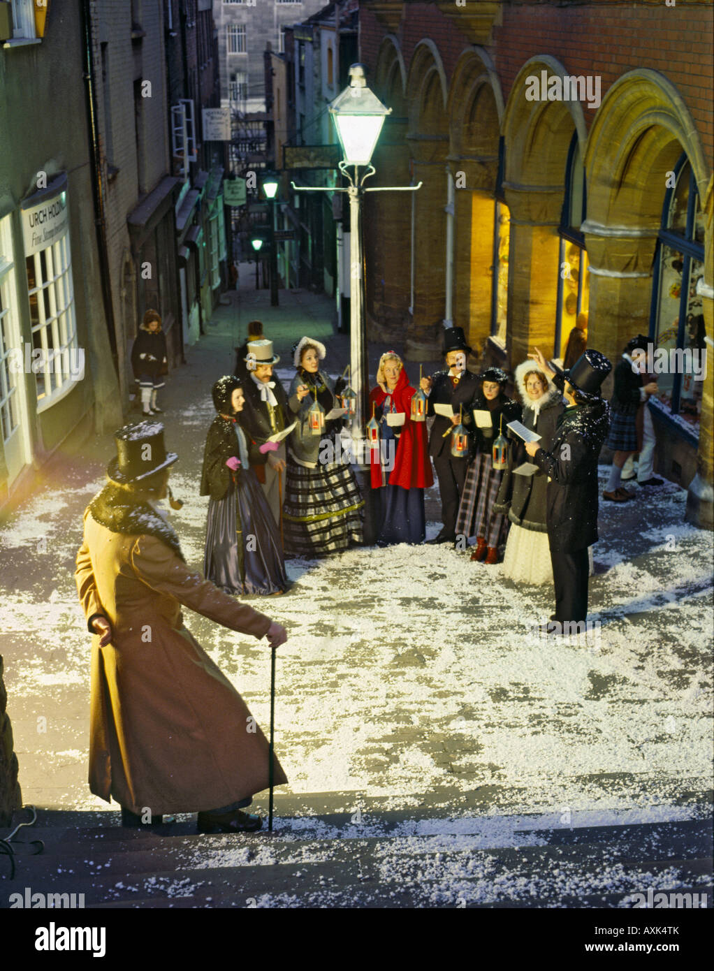 Choir of eight people dressed as Victorian singers at night under old fashioned streetlight at Christmas Steps in Bristol UK Stock Photo