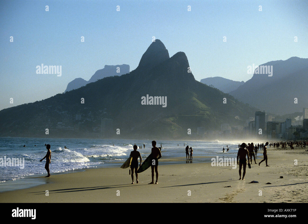 Couple walk with surfboards on Ipanema Beach with sea and unusual shaped hills beyond in Rio De Janeiro Brazil Stock Photo