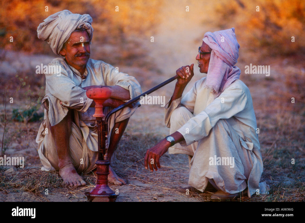 Two Indian men enjoying smoking a opium pipe together at the end of the day at dusk in the countryside near Delhi India Stock Photo