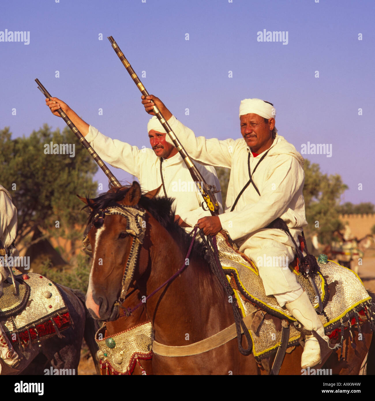 Two Berber horsemen sitting on ornate silver filigree saddles in traditional long white robes & headbands Marrakech Morocco Stock Photo