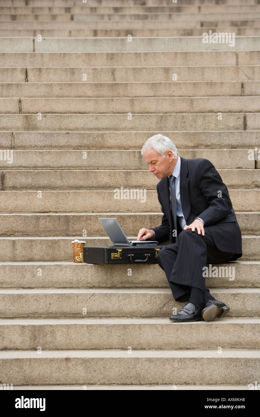 Man sitting outdoors on stairs with laptop Stock Photo