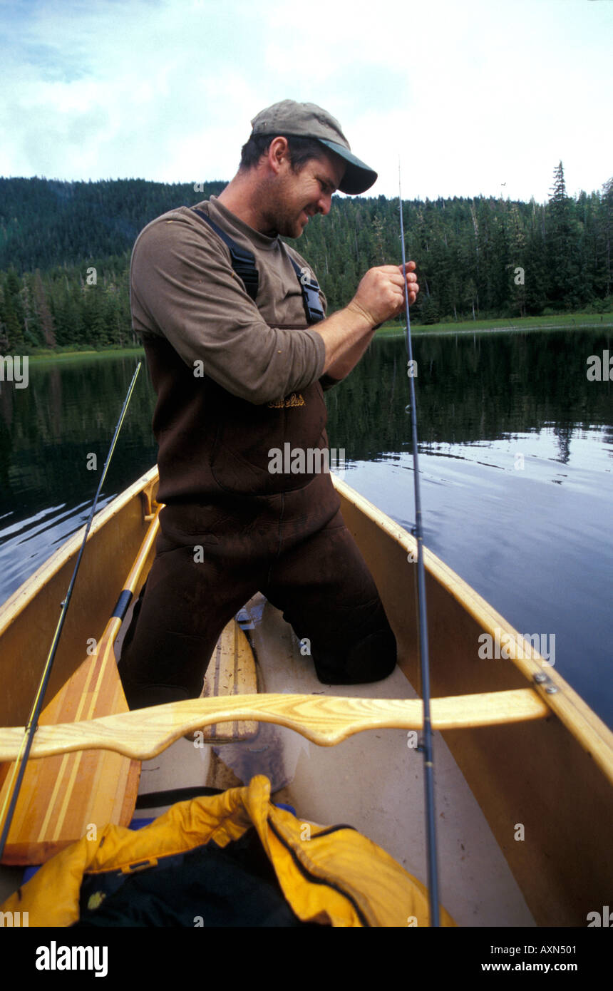 A fly fisherman in waterproof wading pants is kneeling in a canoe