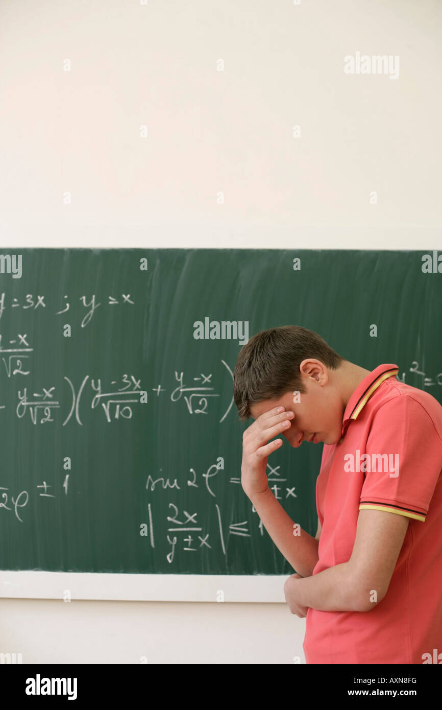 Helpless teenage boy in front of a blackboard with an arithmetic problem Stock Photo
