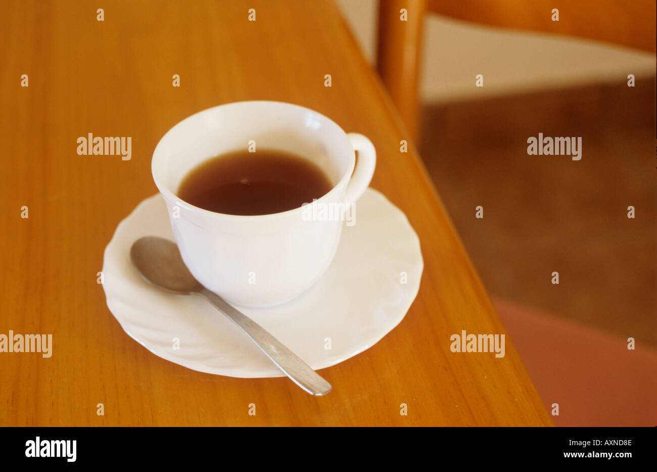 Half full cup of coffee or tea with saucer and teaspoon on a table with an empty chair Stock Photo