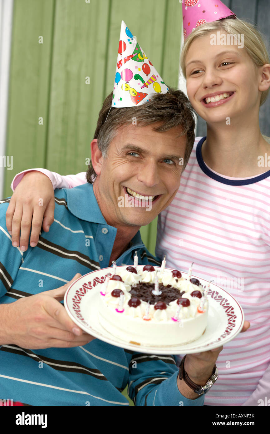 Mature man with a birthday cake in his hand next to his blond daughter