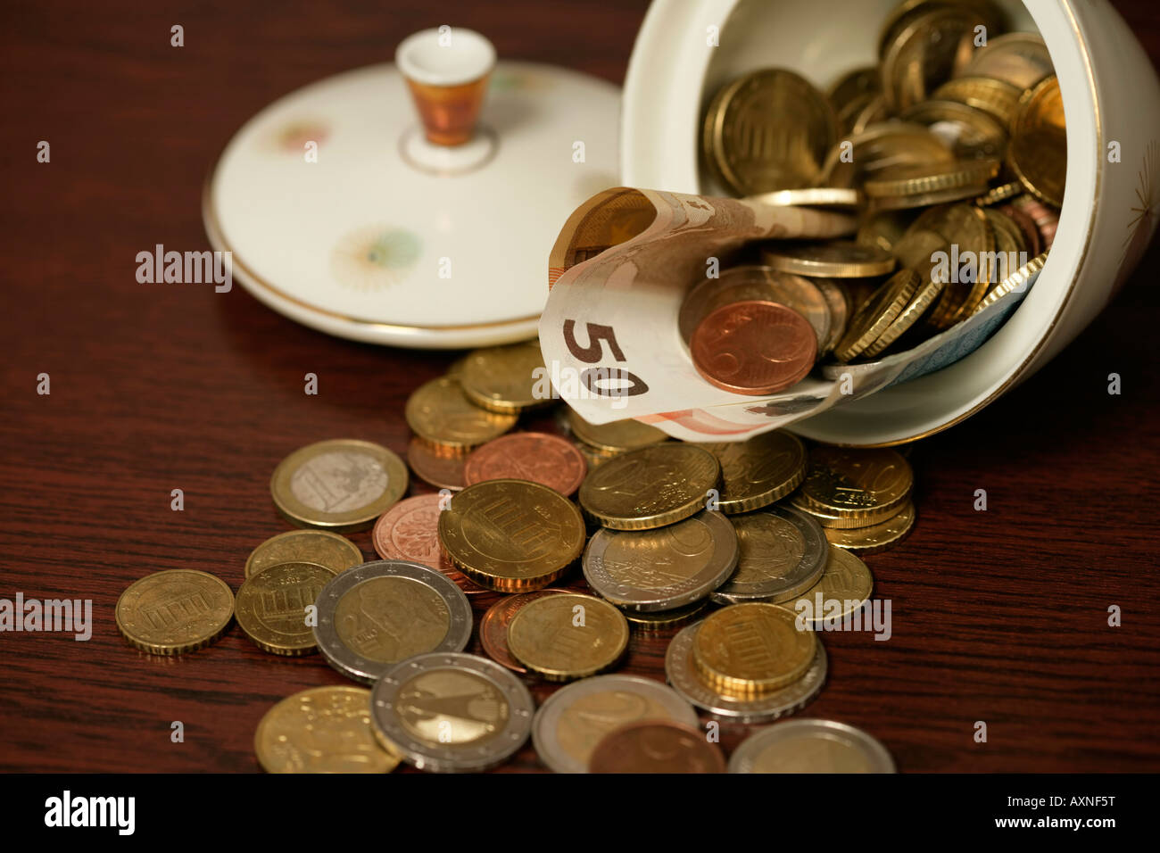 Hand with coins in front of a sugar bowl filled with Euro bills (part of), close-up Stock Photo