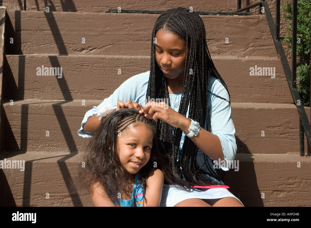 Teenage African American Girl Sitting On Steps And Braiding Hair