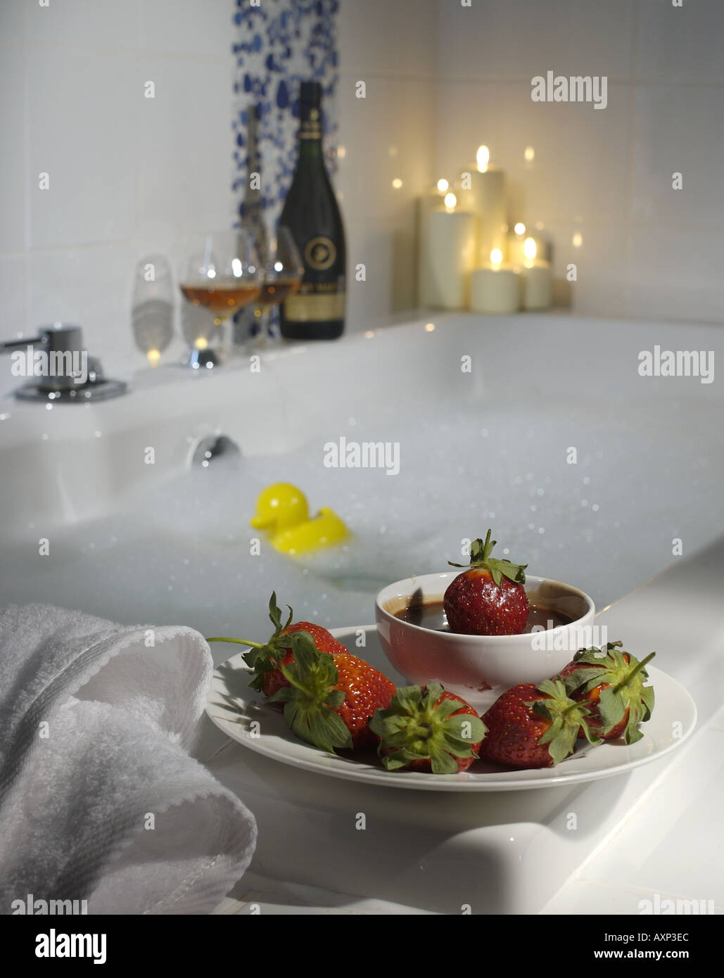 a modern bath room with a bowl for strawberries with chocolate sauce white fluffy towels and cognac candles bubble bath Stock Photo
