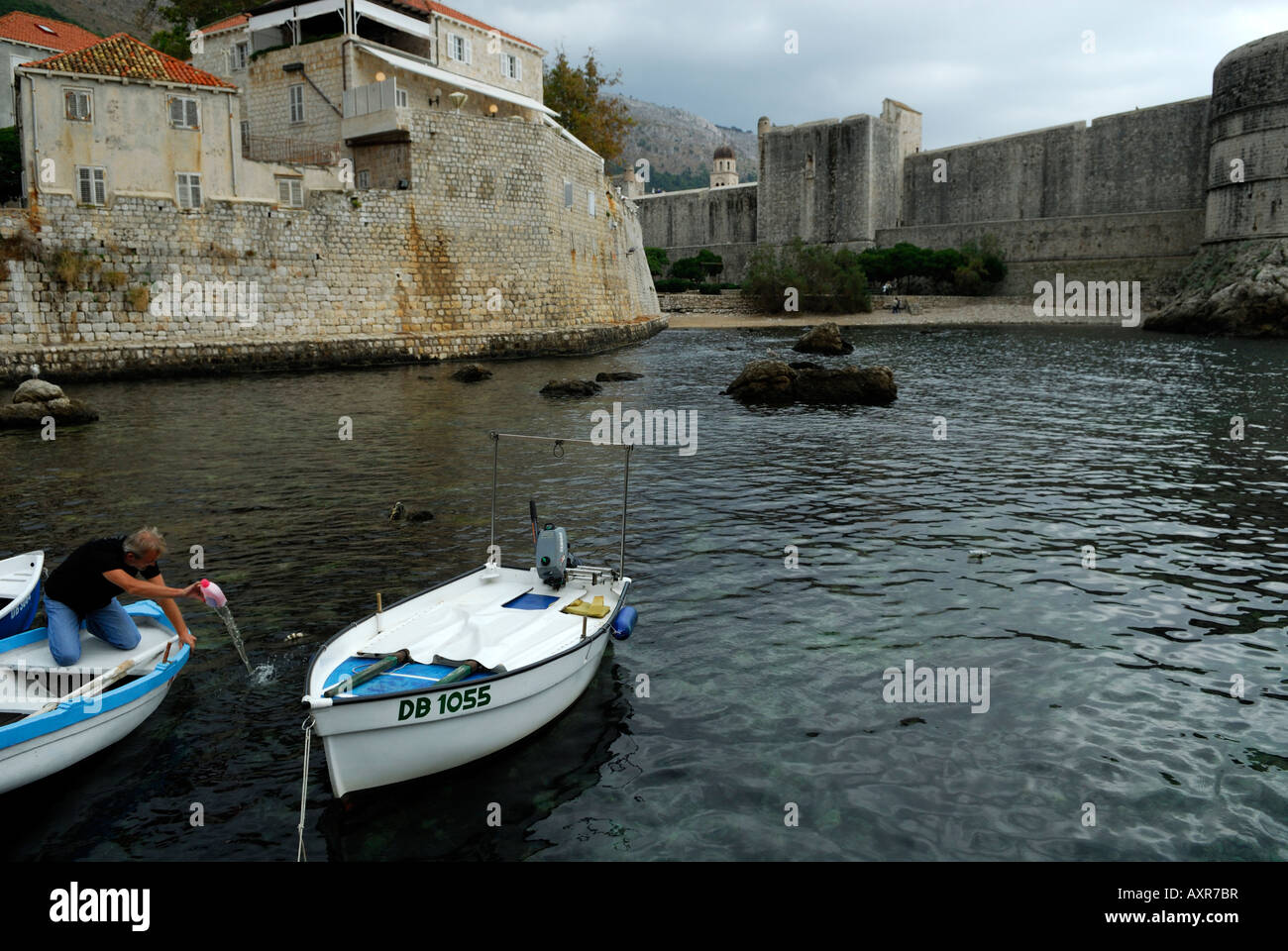 Man emptying water from small boat in Dubrovnik's oldest harbour, Kalarinja. Dubrovnik old town, Croatia Stock Photo