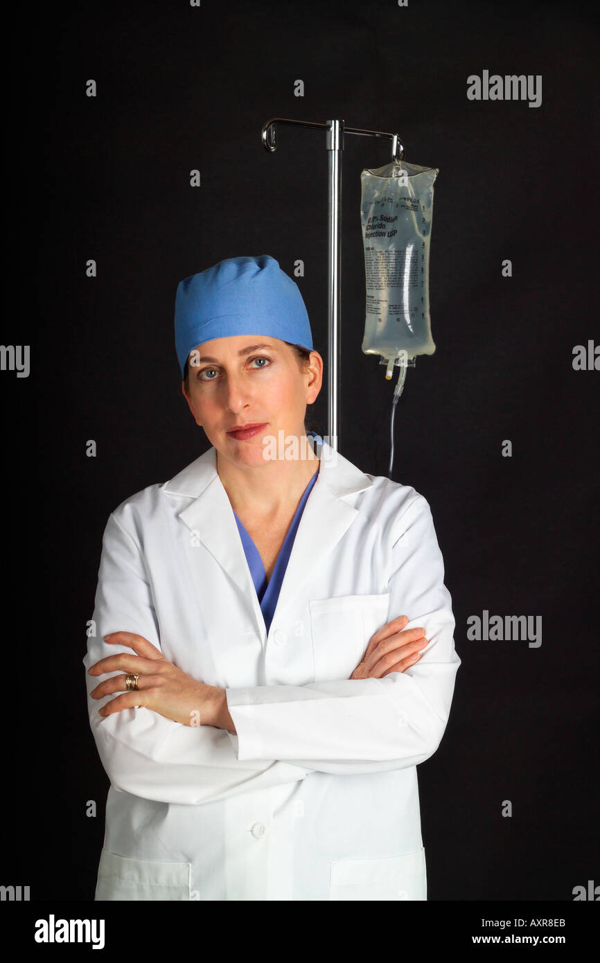 Nurse or doctor wearing surgical scrubs cap and white lab coat stands next to IV stand  Stock Photo