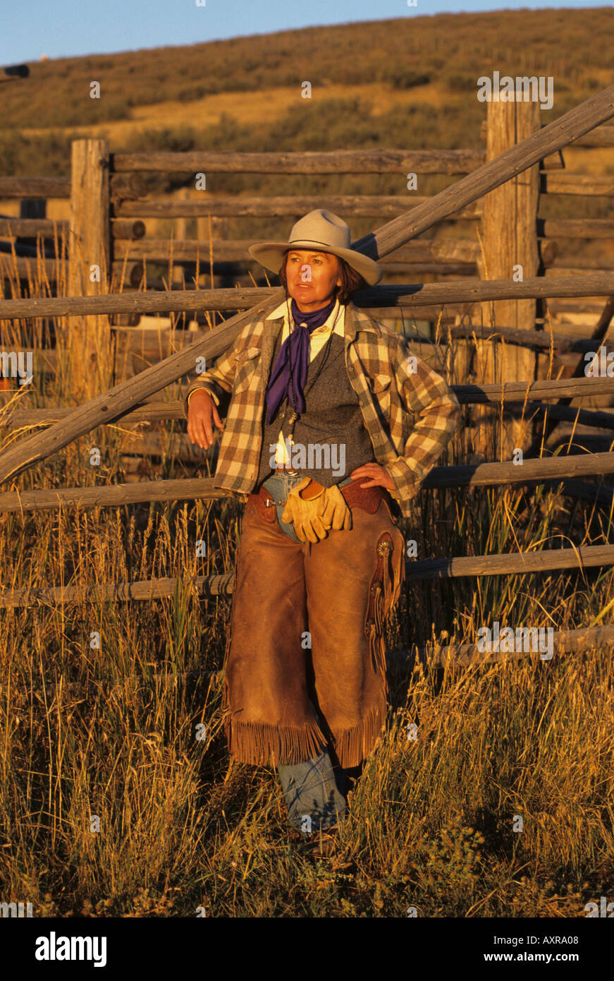 Female rancher in chaps and cowboy hat stands by corrals Stock Photo