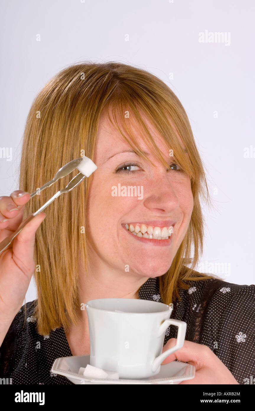 A happy young woman with sugar tongs and sugar cube. Stock Photo