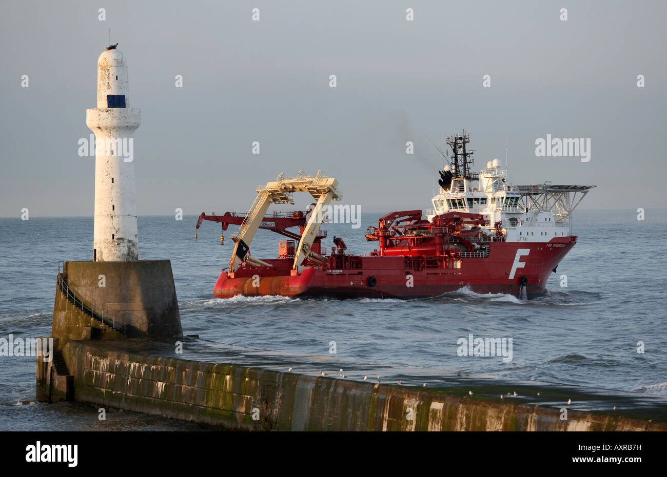 Oil supply vessel passes the breakwater lighthouse as it leaves the harbour at Aberdeen, Scotland, UK Stock Photo
