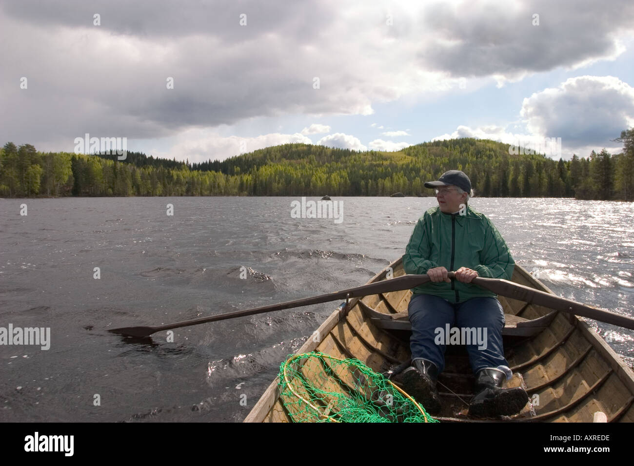 An elderly woman rowing a wooden rowboat  / skiff / dinghy at a lake , Finland Stock Photo