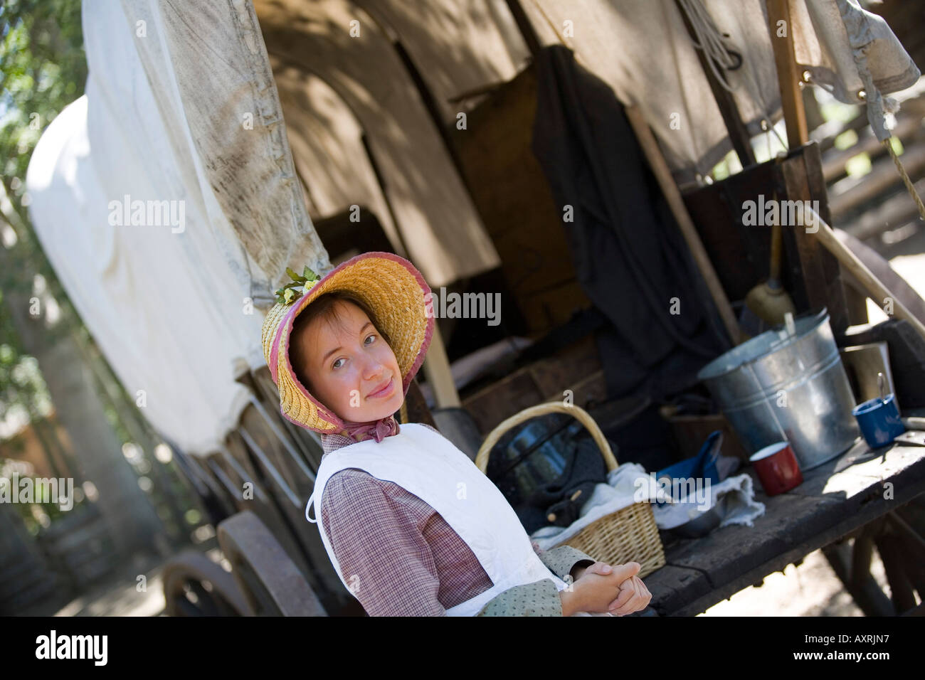 Woman in old fashioned clothing beside covered wagon Stock Photo