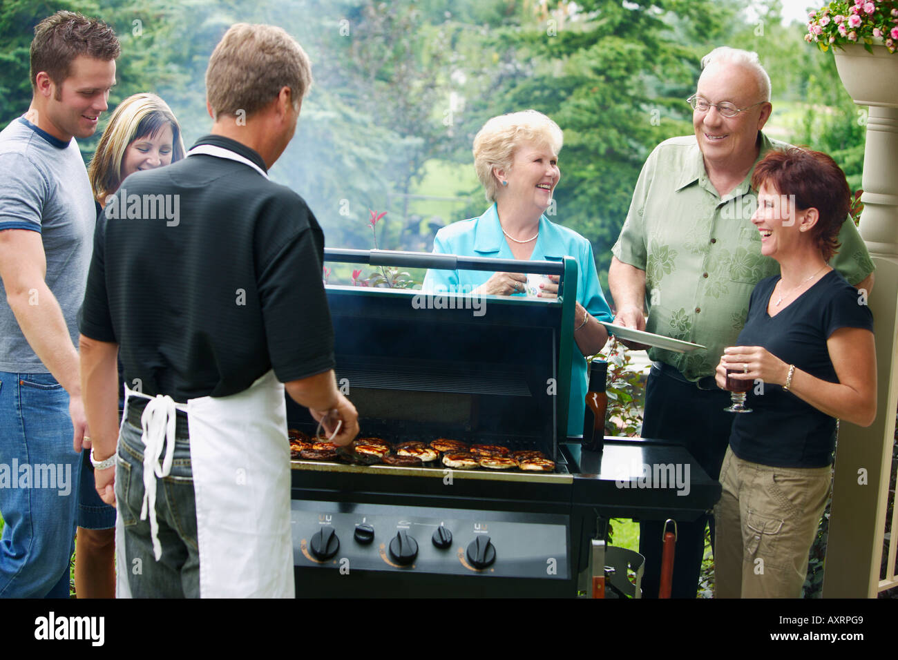 Man barbecuing burgers and talking with group of people Stock Photo