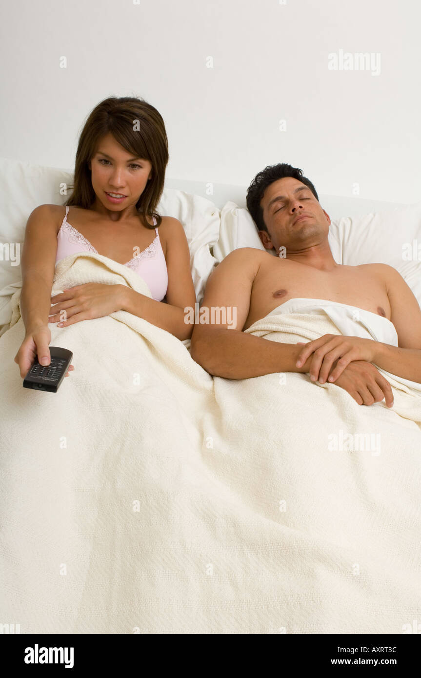 Portrait of a woman watching TV in bed while her husband sleeps Stock Photo  picture photo