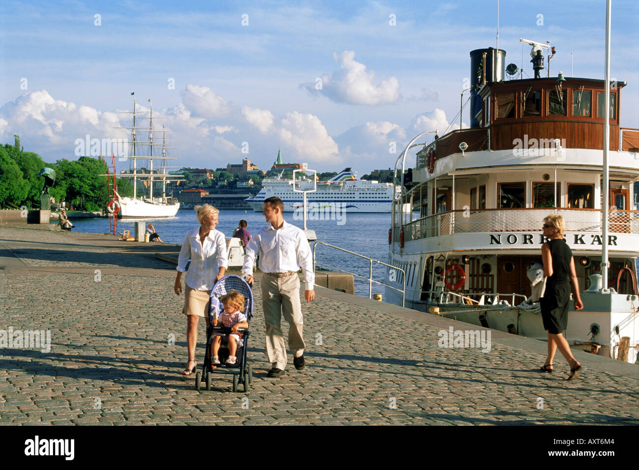 Couple pushing baby carriage at Blasieholmen waterfront in Stockholm with Af Chapman schooner behind Stock Photo