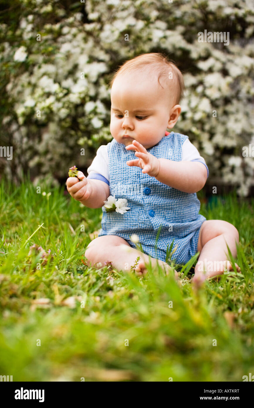 Baby boy sits in grass and looks at a flower during the spring Stock Photo