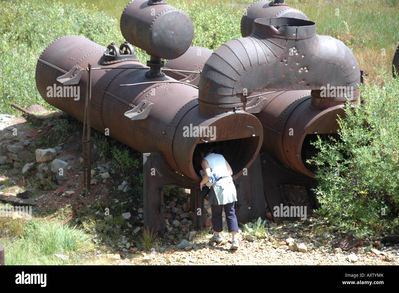 Old mining equipment at Holy Cross City, a Ghost Town, high in the Colorado Rockies. A visitor investigates the interior of an abandoned double boiler. Stock Photo