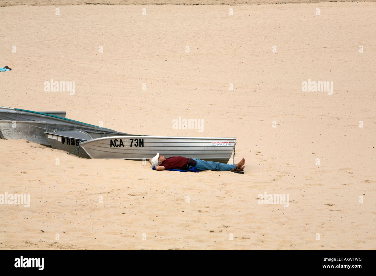 Man lying down beside dinghies on coogee beach,sydney,australia Stock Photo