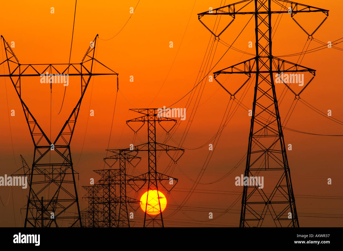 Power lines and setting sun represent two options for meeting power demand Stock Photo