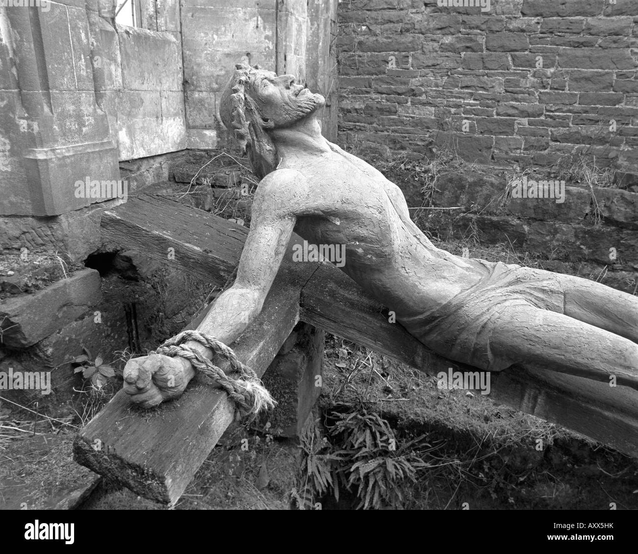 Black and white picture of statue of Jesus on a wooden cross abandoned in the ruins of Brougham Hall in Cumbria Stock Photo