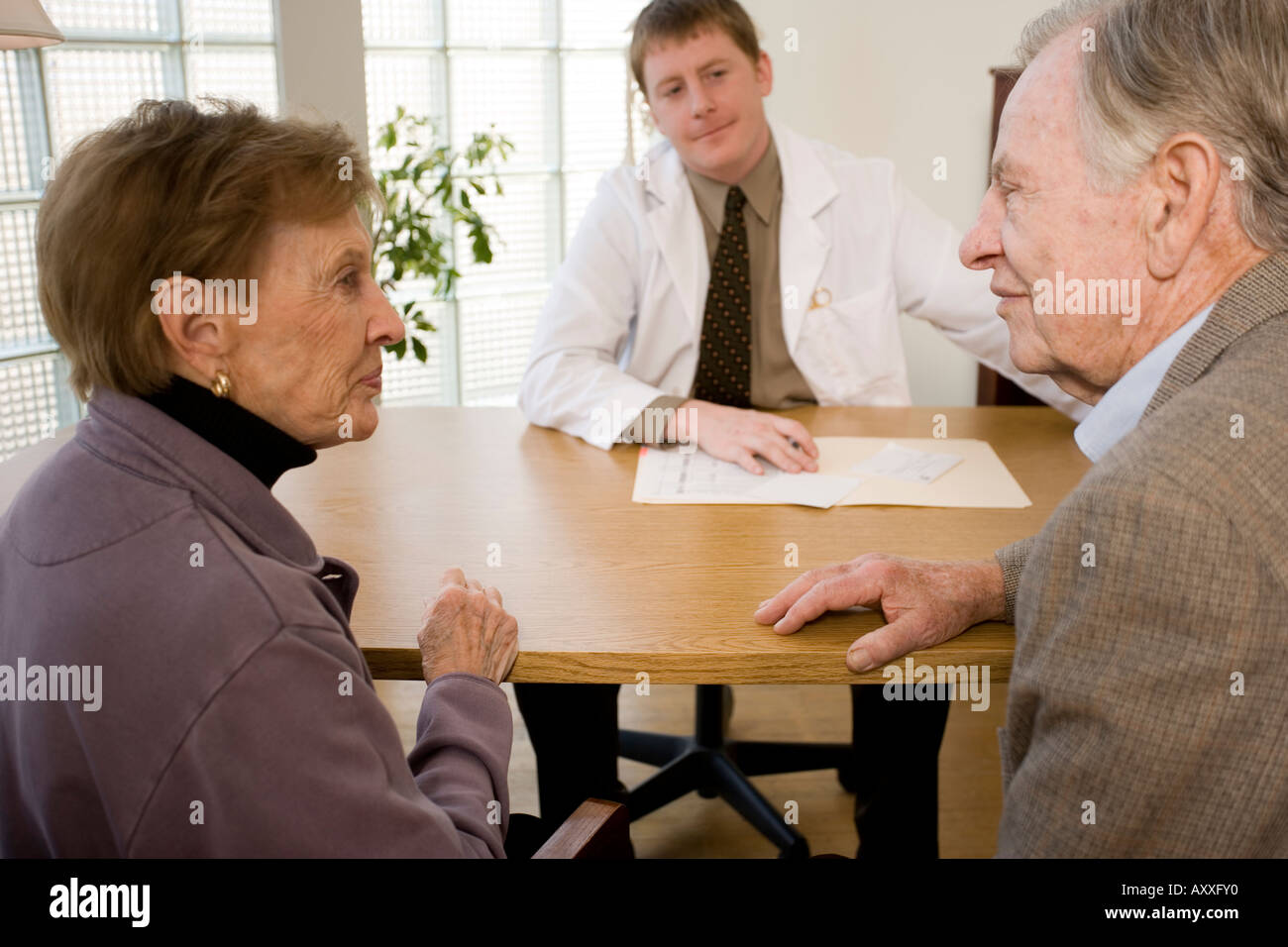 Male patient consults with his doctor (psychiatrist, psychologist,surgeon or primary care physician) as his wife looks on. Stock Photo